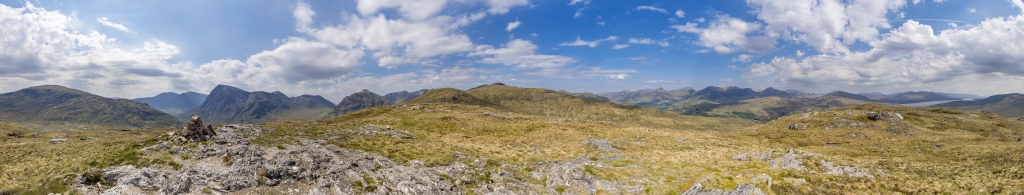360-Grad-Gipfelpanorama auf dem Beinn Bheag (616m) mit Blick auf den Stob Dearg (1021m), den Stob Coire Reineach (925m), den Stob Mhic Mhartuin (716m) und den grasigen Kamm des Sron Garbh (873m) und Meall Dearg (953m) - Fernsicht bis hinüber zum wolkenfreien und langgezogenen Gipfel des Ben Nevis (1345m), im Nordosten das Blackwater Reservoir, Schottland, Mai 2024.