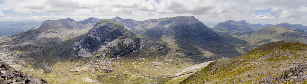 Panorama am Gipfel des Meall a Ghiubhais (887m) mit Blick auf den langen Kamm des Beinn Eighe Massivs mit seinen einzelnen Gipfeln und seinen höchsten Erhebungen des Spidean Coire Nan Clach (977m) und des Ruad-Stac Mor (1010m), den wuchtigen sich davor erhebenden Ruadh-Stac Beag (896m), den weiter entfernten Kamm des Liathach mit der höchsten Gipfelerhebung des Spidean a Choire Leith (1055m), das Hochplateau des Beinn a Chearcaill (725m) mit dem dahinter aufragenden Beinn an Eoin (855m), Torridon Mountains, Schottland, Juni 2024.